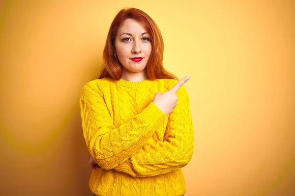 美丽的红头发女人 穿着冬季毛衣 站在孤立的黄色背景上 手指头指向广告的侧面 严肃而镇定的面孔 — 图库照片