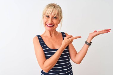 Orta yaş kadın rahat çizgili t-shirt izole beyaz arka plan üzerinde duran giyen hayran ve el ile sunarken kameraya gülümseyerek ve parmak ile işaret.