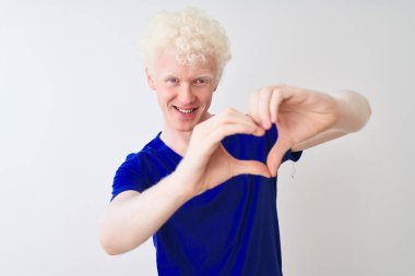 Genç albino sarışın adam mavi rahat t-shirt giyen izole beyaz arka plan üzerinde sevgi kalp sembolü ve elleriyle şekil gösteren gülümseyerek ayakta. Romantik kavram.