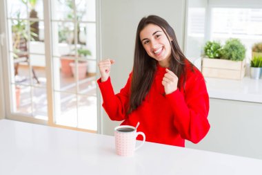 Güzel genç kadın çok mutlu ve heyecanlı kollarını kaldırdı, gülümseyerek ve başarı için çığlık ile kazanan jest yapıyor bir fincan siyah kahve içme. Kutlama konsepti.