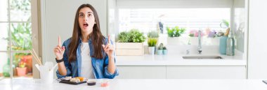 Teslimat suşi yiyen güzel genç kadın geniş açılı resim şaşırttı ve baktı ve parmakları ile işaret ve kolları kaldırdı şaşırttı.