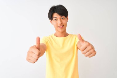 Izole beyaz arka plan üzerinde duran sarı rahat t-shirt giyen Çinli adam el ile olumlu jest yapıyor onaylayan, gülümseyerek kadar başparmak ve başarı için mutlu. Kazanan jest.