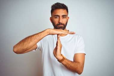 İzole beyaz arka plan üzerinde duran t-shirt giyen genç hintli adam elleri ile zaman dışarı jest yapıyor, sinirli ve ciddi yüz