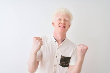 Genç albino sarışın adam izole beyaz arka plan üzerinde duran rahat gömlek giyen çok mutlu ve heyecanlı kolları kaldırdı ile kazanan jest yapıyor, gülümseyerek ve başarı için çığlık. Kutlama konsepti.