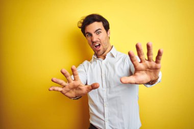 Zarif gömlek giyen genç işadamı izole sarı arka plan üzerinde duran korkmuş ve korku ifade ile korkmuş elleriyle jest durdurmak, şok içinde bağırarak. Panik kavramı.