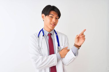 Yüzünde büyük bir gülümseme ile izole beyaz arka plan üzerinde ceket kravat ve stetoskop giyen Çinli doktor adam, kameraya bakarak yan el ve parmak ile işaret.