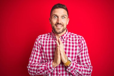 Genç ve yakışıklı bir adam izole edilmiş arka planda ellerini birleştirip af diliyor kendinden emin bir şekilde gülümsüyor..