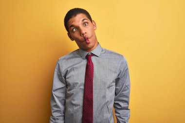 Genç, yakışıklı Arap iş adamı gömleği ve kravat takıp izole edilmiş sarı arka planda balık suratlı, çılgın ve komik bir jest yapıyor. Komik ifade.