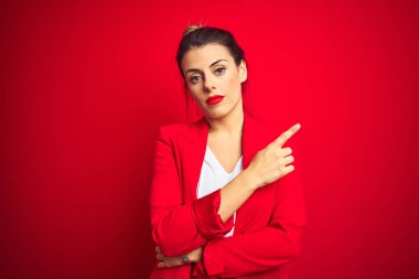 Genç ve güzel bir iş kadını kırmızı izole edilmiş arka planda duruyor. Elleriyle işaret ediyor. Reklamını yapıyor, ciddi ve sakin bir yüz.
