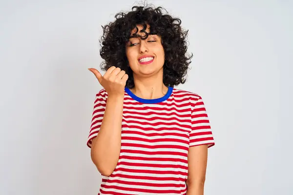 年轻的阿拉伯妇女与卷发穿条纹T恤在孤立的白色背景微笑与幸福的脸看 并指着一边竖起大拇指 — 图库照片