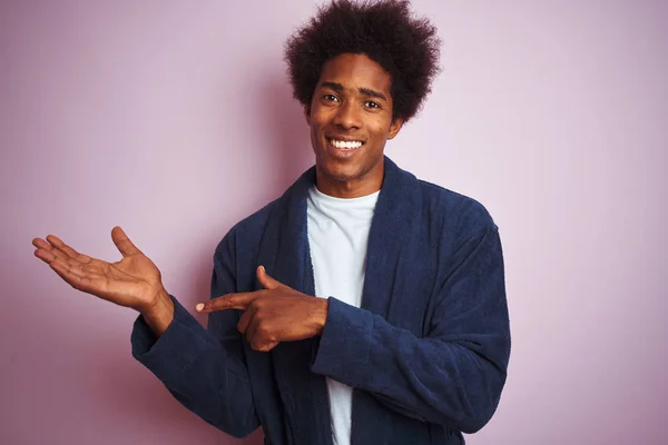 孤立したピンクの背景の上に立つパジャマを着た若いアフリカ系アメリカ人男性は 手を差し伸べ 指で指を向けながらカメラに驚き 微笑んでいます — ストック写真