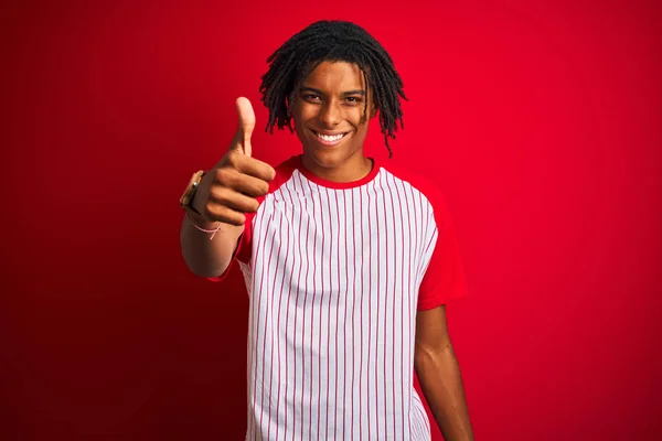 非洲男子穿着条纹T恤 站在孤立的红色背景上 用手竖起大拇指 做着快乐的手势 批准表达式 以显示成功的相机 — 图库照片