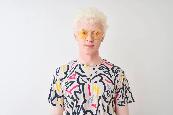 Young albino blond man wearing colorful t-shirt and sunglasses over isolated red background with serious expression on face. Simple and natural looking at the camera.