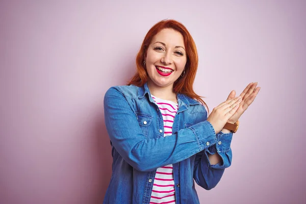 Beautiful redhead woman wearing denim shirt and striped t-shirt over isolated pink background clapping and applauding happy and joyful, smiling proud hands together