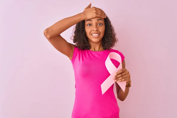 孤立したピンクの背景の上に立って癌のリボンを保持する若いブラジルの女性が頭の上に手で強調し 恥と驚きの顔でショックを受け 怒りと不満 恐怖と過ちへの動揺 — ストック写真