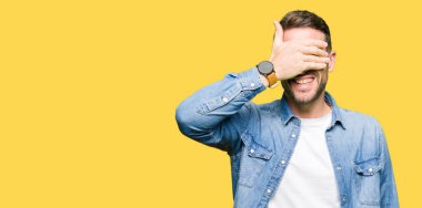 Denim ceket gülümseyen ve gözler için sürpriz kapsayan yüz el ile gülüyor sakal ve mavi gözlü yakışıklı adam. Kör kavramı.