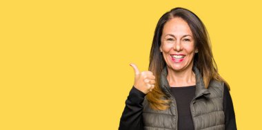 Hareketi el ile mutlu yaşasın yapıyor kış yelek giyen güzel orta yaş kadın. Başarı gösteren kameraya bakarak ifade onaylama.