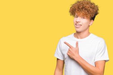 Afro saç ile genç yakışıklı adam rahat beyaz t-shirt yüz üzerinde mutlu ve doğal ifade ile yan el ve parmak ile işaret yüzü bir gülümseme ile neşeli giyiyor