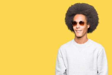 Afro saçlı Genç Afrikalı Amerikalı adam yüz gülümseme ile yan yana görünümlü güneş gözlüğü giyiyor, doğal ifade. Güven gülüyor.
