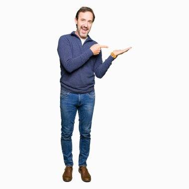 Hayret ve el ile sunulması ve parmak ile işaret ederken kameraya gülümseyen bir kazak giyen orta yaş yakışıklı adam.