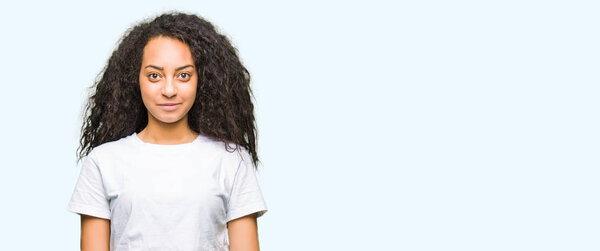 Young beautiful girl with curly hair wearing casual white t-shirt Relaxed with serious expression on face. Simple and natural looking at the camera.