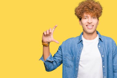 Genç yakışıklı adam afro saç giyen denim ceket gülümseyen ve emin işaret ile el yapıyor boyutu işareti yaparken parmaklar ve kamera bakıyor. Ölçü kavramı.