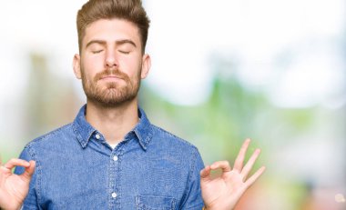 Rahat denim gömlek giyen genç yakışıklı sarışın adam Relax ve gözleri ile gülümseyen meditasyon jest parmaklar ile kapalı. Yoga konsepti.