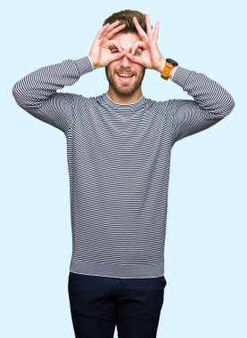 Çizgi kazak giyen genç yakışıklı adam dürbün yapışan gibi ok jest yapıyor, gözleri parmaklarla bakıyor. Çılgın ifade.