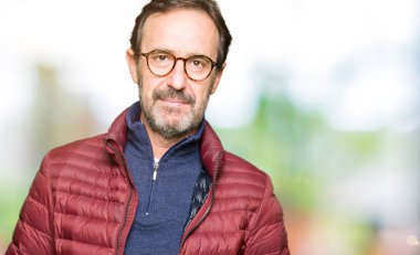 Orta yaş yakışıklı adam gözlük ve kış ceket giyen yüzünde ciddi ifade ile rahat. Kameraya basit ve doğal bir bakış.