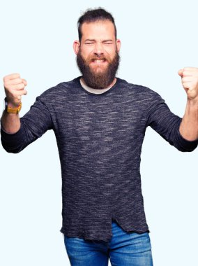 Gülümseyen ve başarı için çığlık rahat kazak çok mutlu ve heyecanlı kaldırdı, silah ile kazanan jest yapıyor giyen genç sarışın adam. Kutlama kavramı.