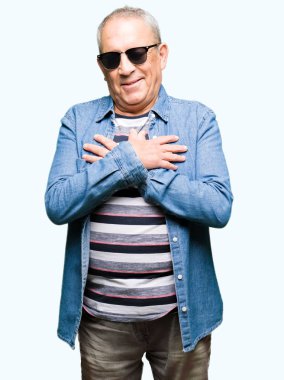 Denim ceket ve ile gülümseyen güneş gözlüğü takan yakışıklı komuta sizde kapalı gözler ve yüzünde minnettar jest ile göğüs üzerinde eller. Sağlık kavramı.