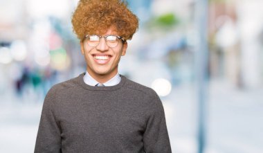 Afro saçlı genç yakışıklı iş adamı yüzünde mutlu ve serin bir gülümseme ile gözlük takıyor. Şanslı kişi.