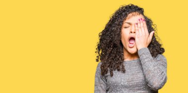 Gri kazak giyen kıvırcık saçlı Genç güzel kadın, el ile yarım yüz, göz ve ağız kapsayan yorgun esneme. Yüz acı acıyor.