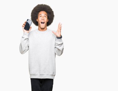 Kocaman bir gülümseme ile çığlık zaferini kutluyor ve ellerini kaldırdı smartphone ekran çok mutlu ve heyecanlı, kazanan ifade gösterilen afro saçlı genç Afro-Amerikan adam
