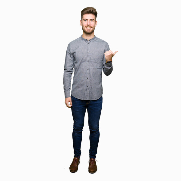 Young handsome business casual man smiling with happy face looking and pointing to the side with thumb up.