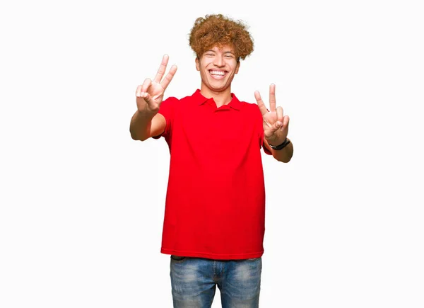 年轻的帅哥 穿着红色T恤微笑着看着镜头显示手指做胜利标志 — 图库照片