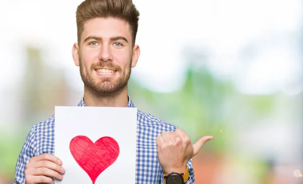 Jovem Homem Bonito Segurando Papel Com Coração Vermelho Apontando Mostrando — Fotografia de Stock