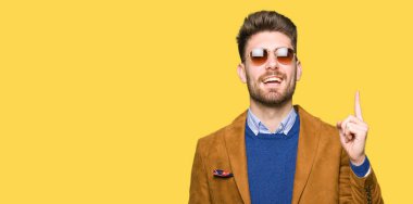 Genç yakışıklı zarif adam başarılı fikirle parmak işaret güneş gözlüğü takıyor. Çıktıktan ve mutlu. Bir numara.