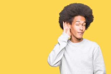 Afro saç ile genç Afrikalı Amerikan adam spor Sweatshirt kulak üzerine el ile gülümseyen söylenti ya da dedikodu bir işitme dinliyor. Sağırlık konsepti.