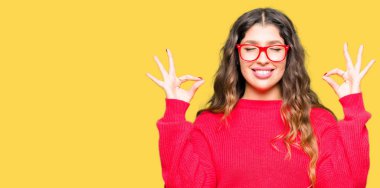 Genç güzel kadın kırmızı gözlük rahatla ve gülümseyen gözlerle kapalı parmak jestle meditasyon yapıyor. Yoga kavramı.