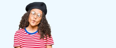 Kıvırcık saçlı, gözlüklü, bereli, dudağından balık suratı yapan, çılgın ve komik bir jest yapan genç bir kadın. Komik ifade.