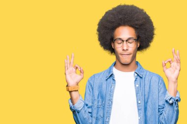 Afro saçlı gözlüklü genç Afro-Amerikan adam rahatla ve gülümseyen gözlerle kapalı parmak jestle meditasyon yapıyor. Yoga kavramı.