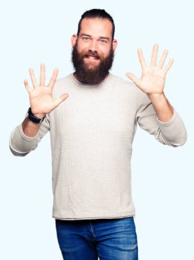 Genç sarışın adam rahat kazak gösteren ve parmak numarası on ile işaret giymiş iken emin ve mutlu gülümseyen.