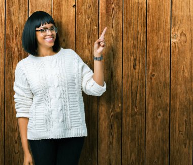 Kameraya bakarak yan el ve parmak ile işaret yüzünde kocaman bir gülümseme ile izole arka plan üzerinde gözlük güzel genç Afro-Amerikan kadın.