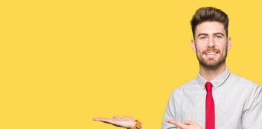 Hayret ve el ile sunulması ve parmak ile işaret ederken kameraya gülümseyen genç yakışıklı iş adamı.