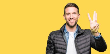 Yakışıklı adam kış ceket gösterme ve parmakları ile işaret giyen üç kendinden emin ve mutlu gülümseyerek iken numara.