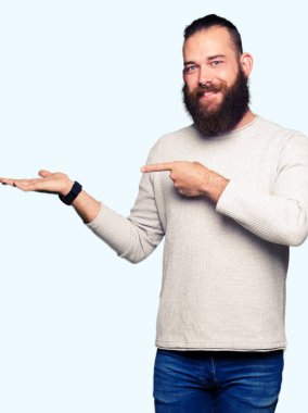 Genç Sarışın giyen sıradan kazak hayret ve el ile sunulması ve parmak ile işaret ederken kameraya gülümseyen adam.