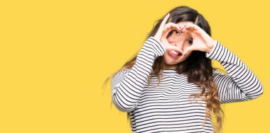 Çizgili süveter yapıyorsun kalp şekli el ve parmak işareti seyir gülümseyen ile giyen genç güzel kadın