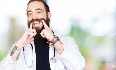 Doktor stetoskop tıbbi ceket giyen uzun saçlı açık ağız ile gülümseyen, işaret ve neşeli zorla parmak gülümse