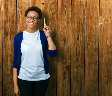 Genç güzel Afrikalı-Amerikalı kadın ve kendinden emin ve mutlu gülümseyerek süre parmak numaralı yukarıyı gösteren izole arka plan üzerinde gözlük.